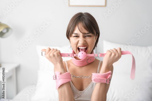 Young woman in handcuffs and with mouth gag from sex shop in bedroom photo