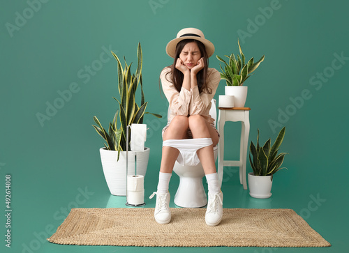 Foto Young woman suffering from diarrhea while sitting on toilet bowl against green b
