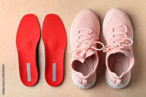 Pair of sportive shoes and red orthopedic insoles on color background