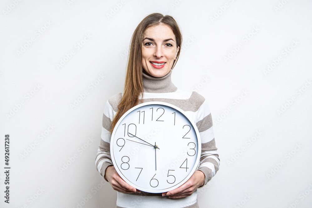 Smiling young woman holding white wall clock on light background. Smiling young woman holding white wall clock on light background.