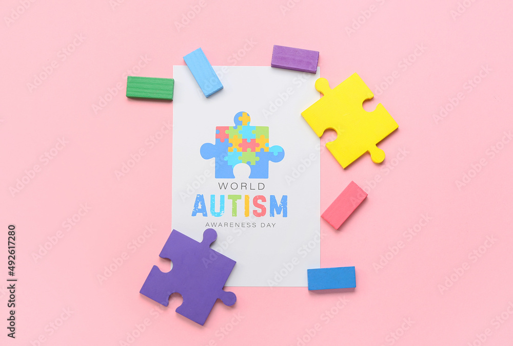 Paper sheet with text WORLD AUTISM AWARENESS DAY, puzzle pieces and blocks on pink background Paper sheet with text WORLD AUTISM AWARENESS DAY, puzzle pieces and blocks on pink background