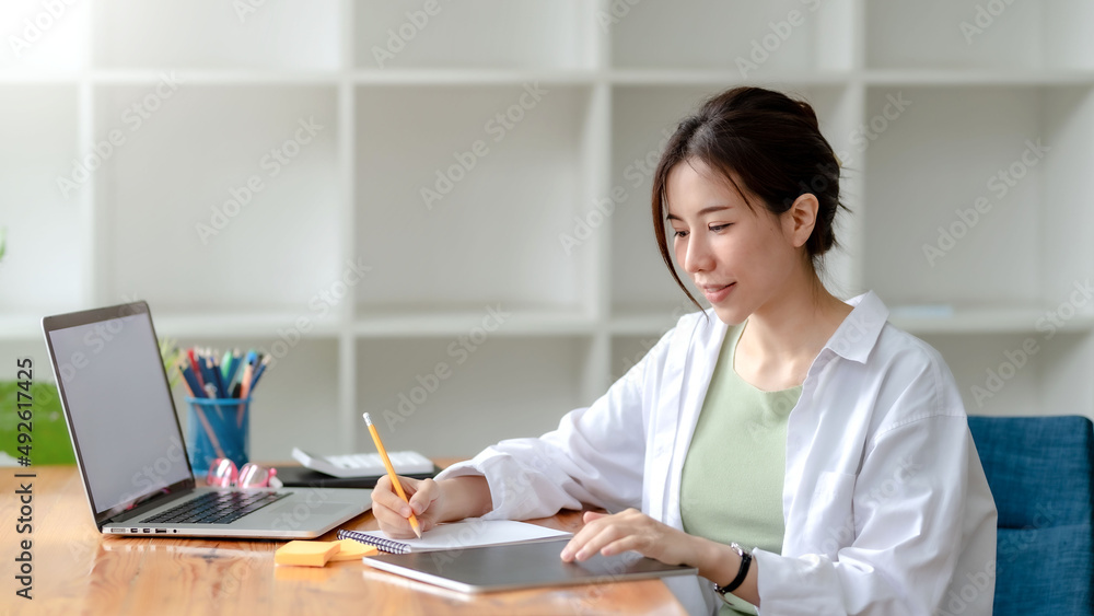 Young Asian businesswoman sitting and taking notes in office. Female student sitting in the library doing homework at home. Young Asian businesswoman sitting and taking notes in office. Female student sitting in the library doing homework at home.