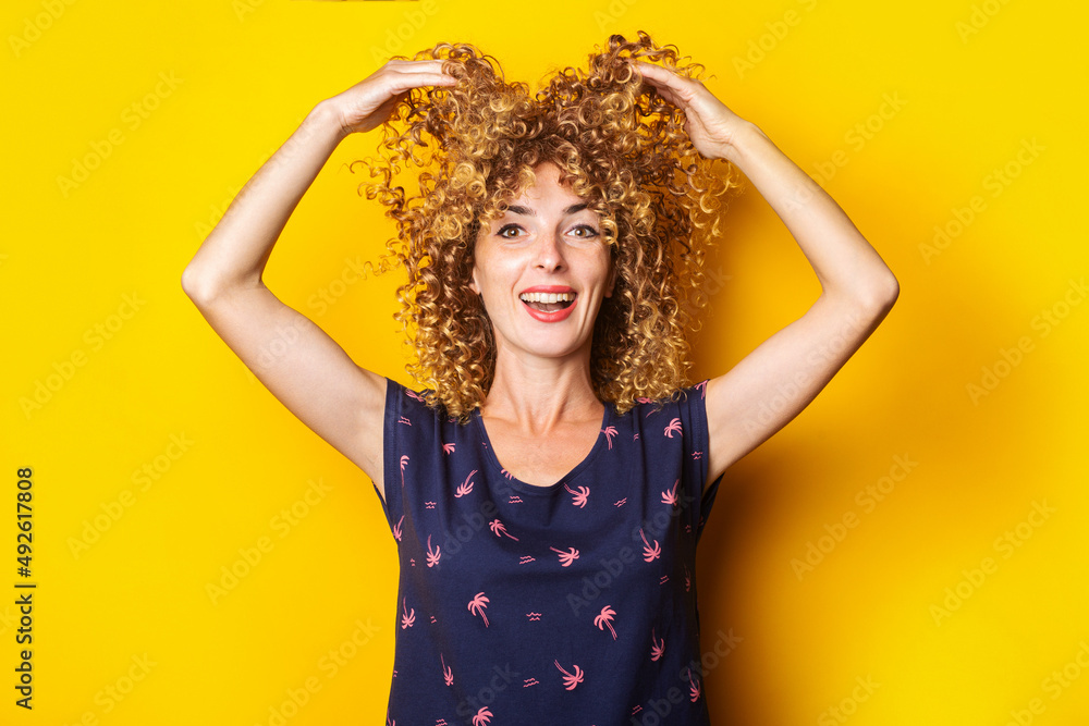 cheerful curly young woman lifts her hair up on a yellow background cheerful curly young woman lifts her hair up on a yellow background