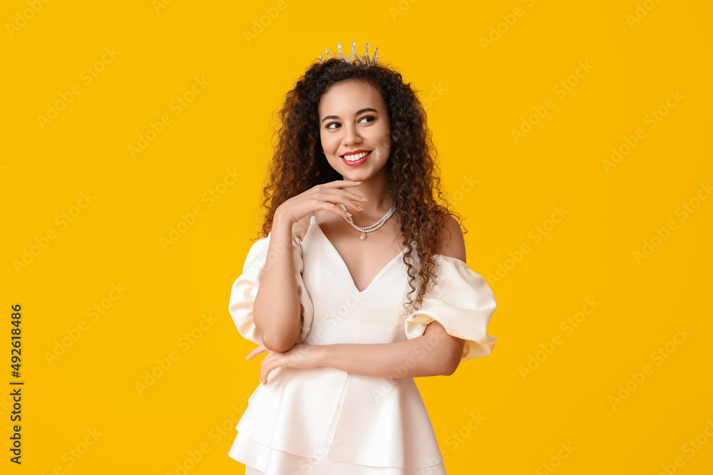 Beautiful young African-American woman in stylish dress and tiara on yellow background Beautiful young African-American woman in stylish dress and tiara on yellow background