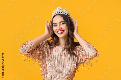 Beautiful young woman in stylish dress and tiara on yellow background photo