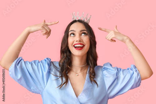 Beautiful young woman in stylish dress and tiara on pink background photo