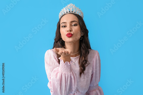 Canvas-taulu Beautiful young woman in stylish dress and tiara blowing kiss on blue background