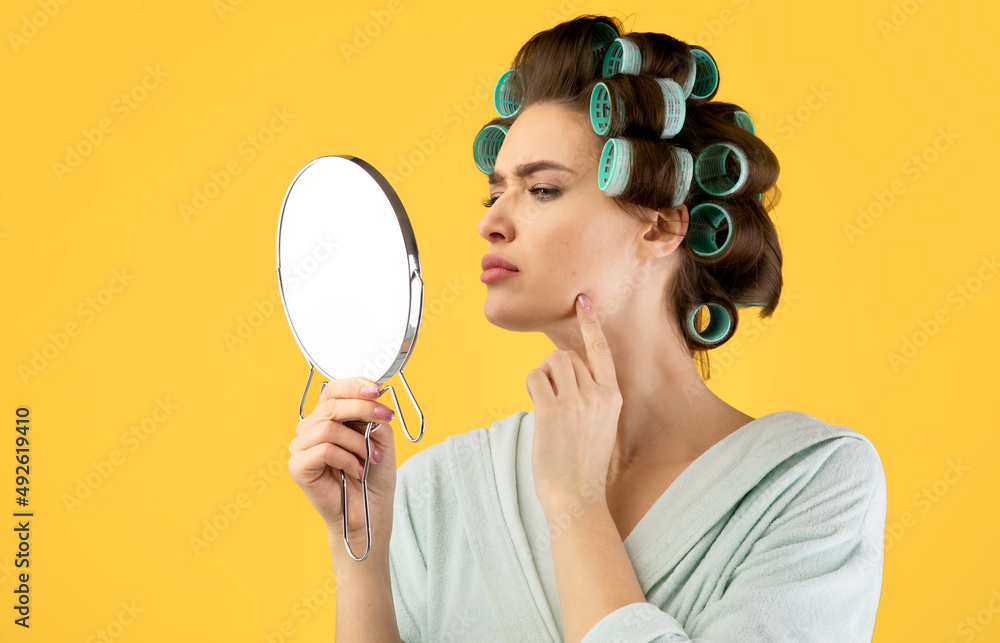 Lady Touching Face Having Pimples Looking In Mirror, Yellow Background Lady Touching Face Having Pimples Looking In Mirror, Yellow Background
