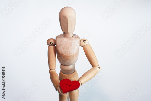 A wooden man holds a red heart in his hands on a light background