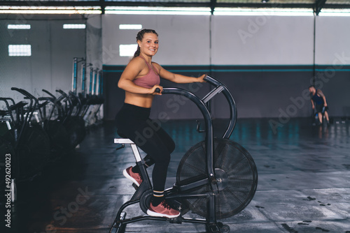 Portrait of cheerful woman training on exercising bike reaching dedication results during intensive cardio training, happy female slimming in modern gym - keeping healthy lifestyle and vitality