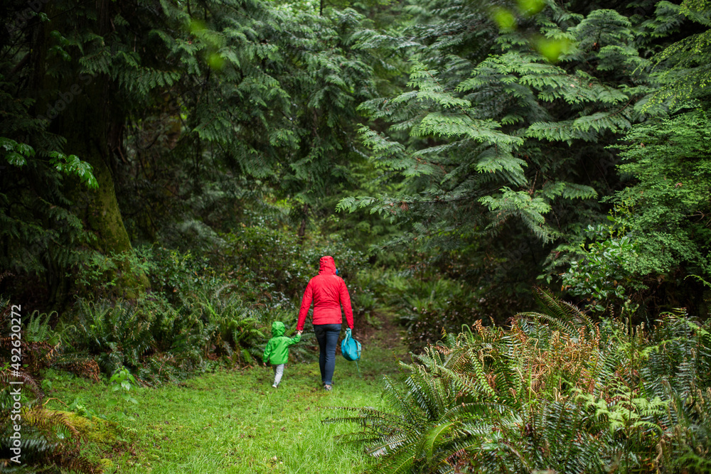 A woman in raincoat walks into forest with young child A woman in raincoat walks into forest with young child