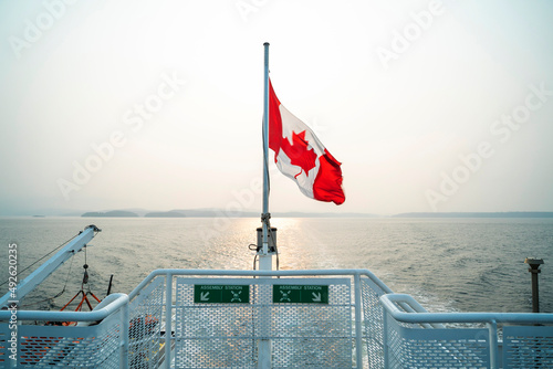 Canadian flag waves at stern of ferry boat over water photo