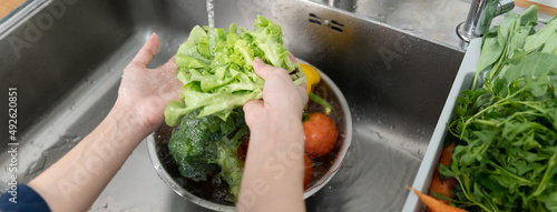 Close up of hands people washing vegetables by tap water at the sink in the kitchen to clean ingredient prepare a fresh salad. photo