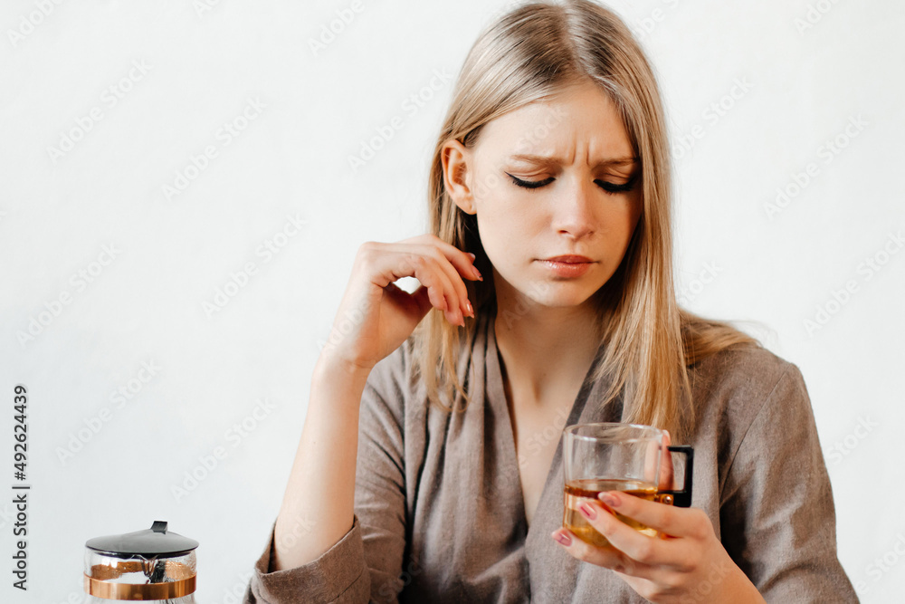 Good-looking girl is suspiciously looking at the glass of tea she is holding. Young woman received a wrong taste of tea. Concept of cafe Good-looking girl is suspiciously looking at the glass of tea she is holding. Young woman received a wrong taste of tea. Concept of cafe
