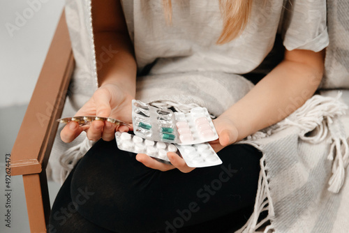 The pills are shown close-up. Young woman is choosing what pills to take. The girl got covid and now she does not feel well. Concept of covid