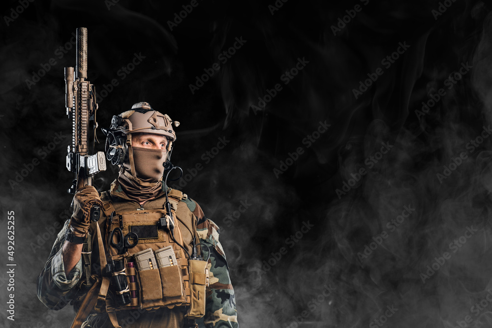 Equipped soldier holding rifle against black background with fog Equipped soldier holding rifle against black background with fog