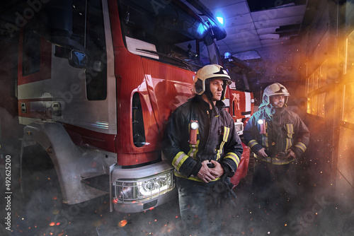 Two firefighters dressed in workwear with helmets in fire station © Fxquadro