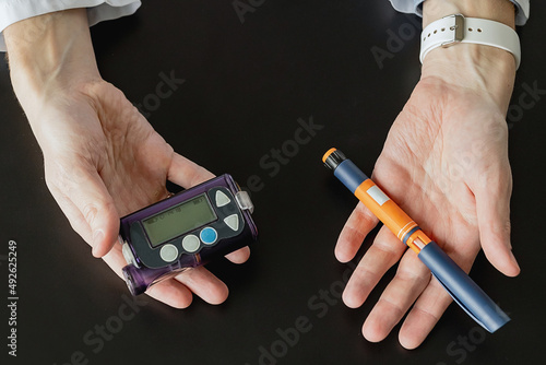 the doctor holds an insulin syringe and an insulin pump in his hands. Diabetes is a disease of the endocrine system. Syringe on a black background. Diabetes treatment choice concept photo