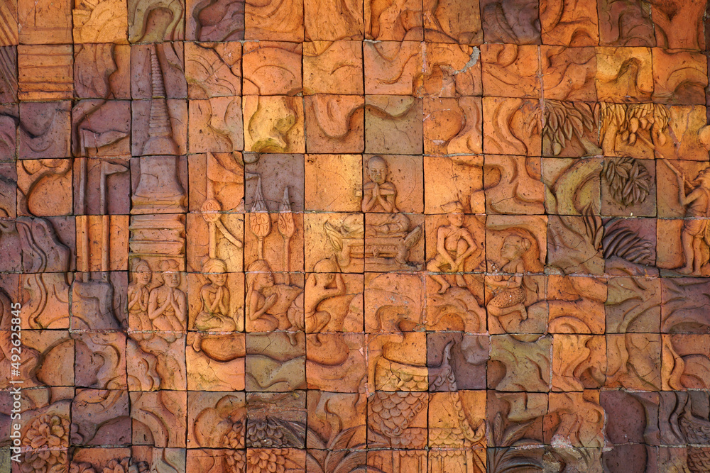 Obraz premium Bas Relief on terracotta tiles wall shows the way of life of Buddhists who listen to the Dharma and raise their hands to pay homage to the monks. The Buddhist way of life in the countryside art.