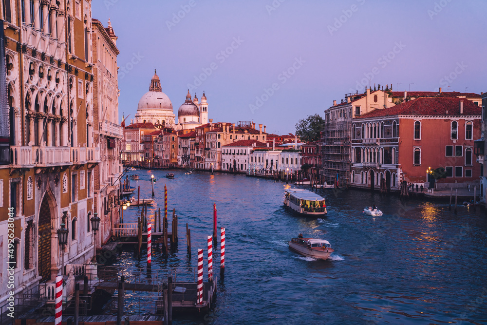 Scenery landscape with motorboat taxi on water of Grand Canal during evening time for romantic sightseeing in Venice, overview on famous architecture buildings during getaway holidays in Italy