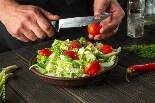 A professional chef prepares a vegetable salad in the restaurant kitchen. Cutting a fresh tomato for a vitamin salad with a knife