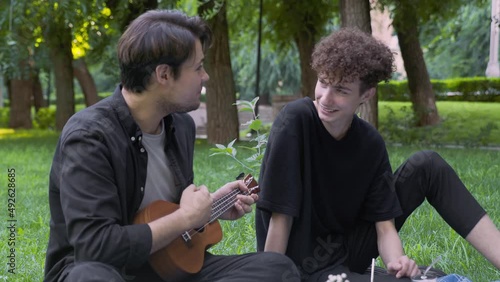 A guy plays the ukulele to another guy in nature in the summer. LGBT