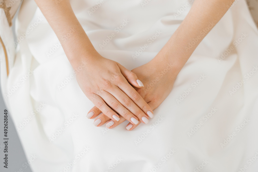 Delicate manicure of the bride, the hands of a young woman lie on a white wedding dress Delicate manicure of the bride, the hands of a young woman lie on a white wedding dress