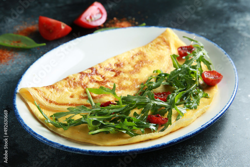 Breakfast. Omelet with arugula and tomatoes on a white plate on a black table. Background image, copy space. Top view, flatlay