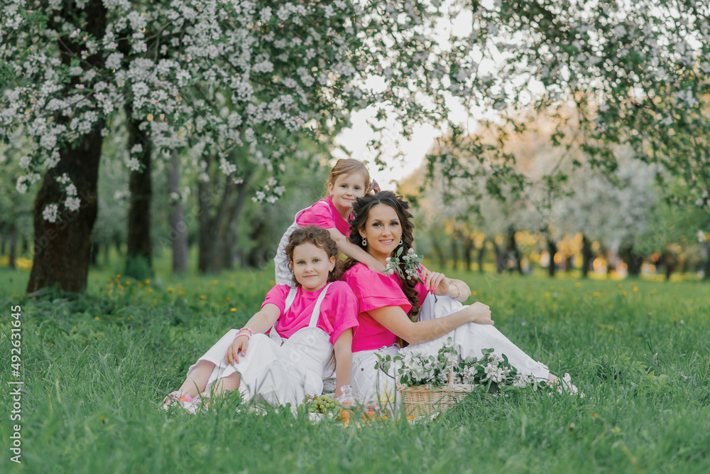 Naklejka premium Cute mom and two daughters are having a picnic in the spring garden. Outdoor activity. Sweet moments family