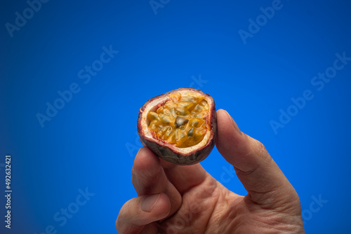 Raw halved maracuya or passion fruits held in hand by Caucasian male. Close up studio shot, isolated on blue background