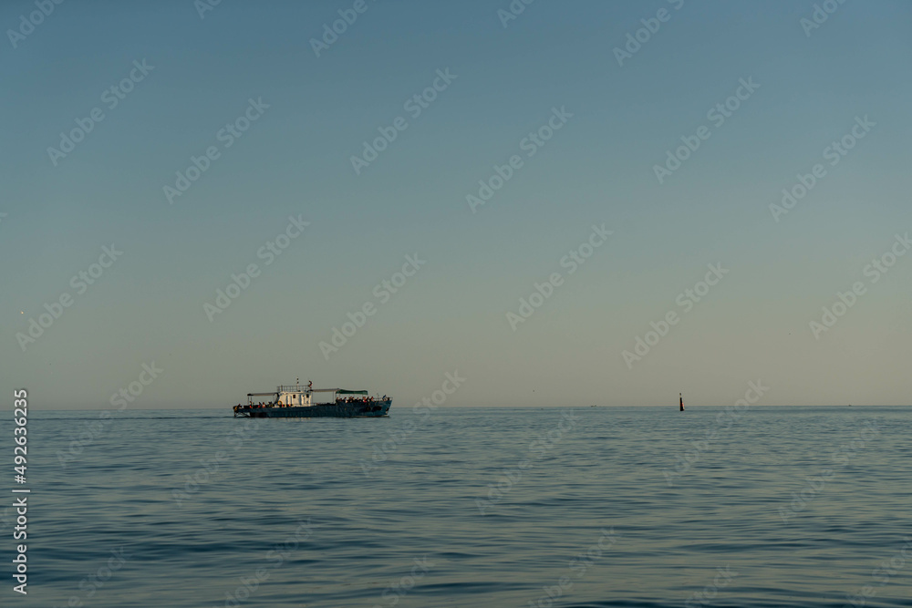 Small marine boat in the sea on the horizon at sunrise.