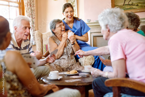 The suspense keeps the game exciting. Shot of a group of happy seniors playing a card game in their retirement home while a nurse watches.
