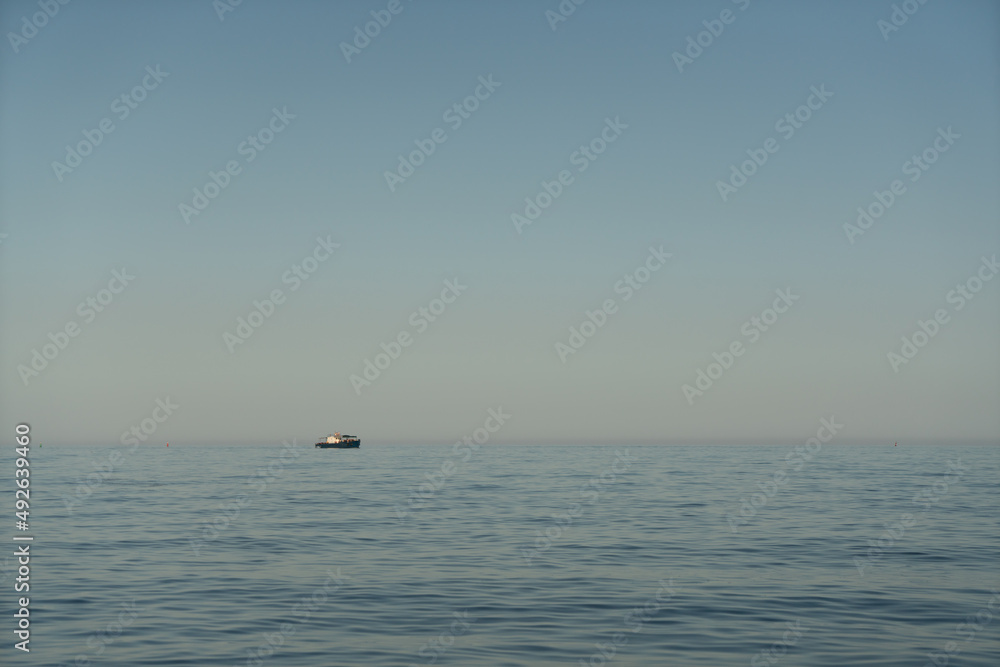 Small marine boat in the sea on the horizon at sunrise.