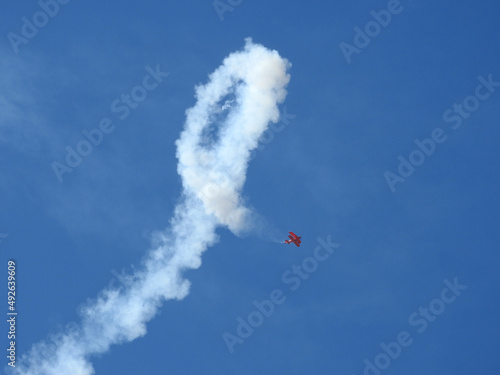 A red biplane performing aerobatic stunts at an airshow in the skies of southern California.