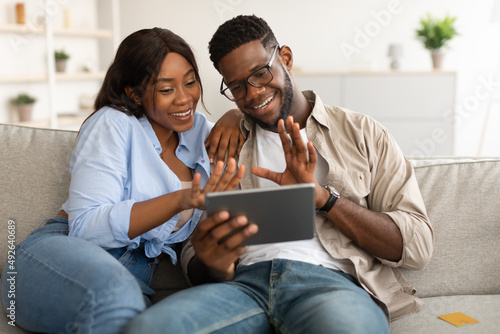 Black couple having videocall using tablet waving hands
