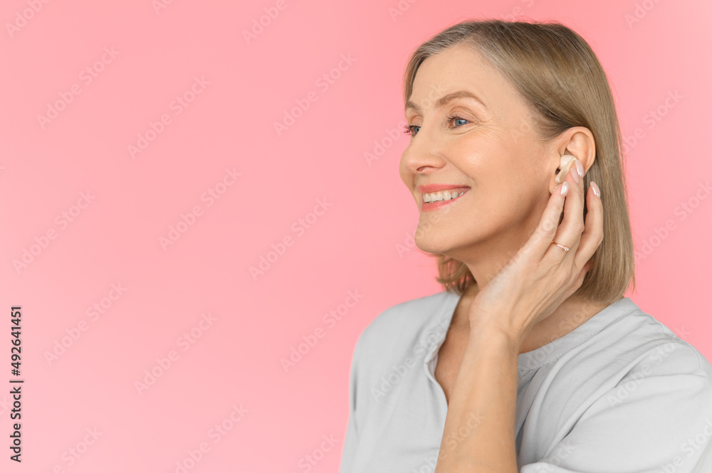 An old woman with Airpods on a pink-rose background. Close up. Portrait of an age woman. An old woman with Airpods on a pink-rose background. Close up. Portrait of an age woman.