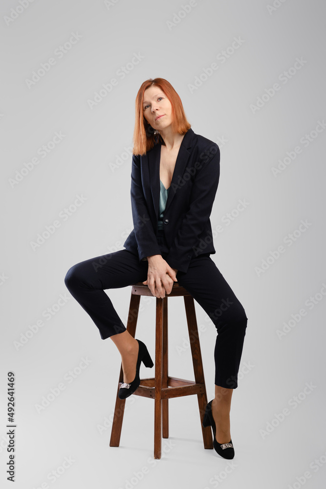 Stylish middle aged woman in pantsuit posing in studio sitting on chair with legs spread Stylish middle aged woman in pantsuit posing in studio sitting on chair with legs spread