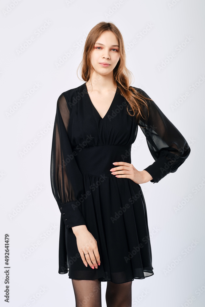 Young woman in little black dress holds one arm on waist, studio shot Young woman in little black dress holds one arm on waist, studio shot