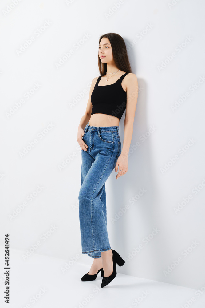 Young woman in black tank top and denim jeans leaning to the wall Young woman in black tank top and denim jeans leaning to the wall