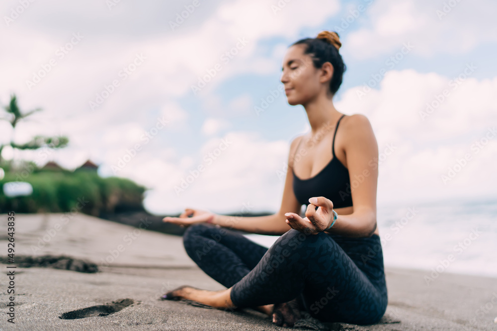 Harmony and meditation training during morning yoga at coastline beach, blurred female in sportswear sitting in lotus pose during aerobic pilates for exercising own body concentration in asana