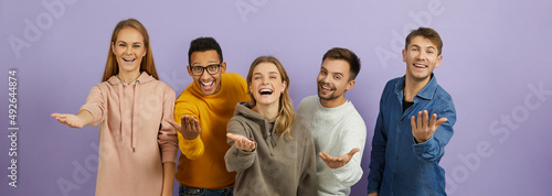 Team of happy positive cheerful joyful young multiethnic people standing together, looking at camera, smiling, reaching out hands and doing inviting gesture, telling you 'Come here and join us'