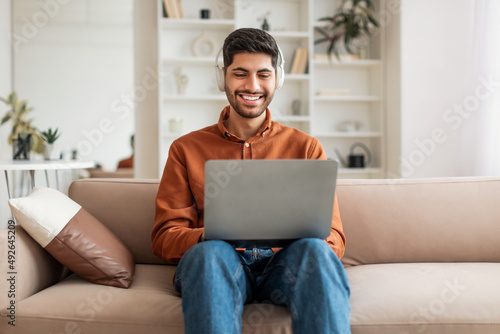 Smiling Arab man using pc at home, listening to music © Prostock-studio