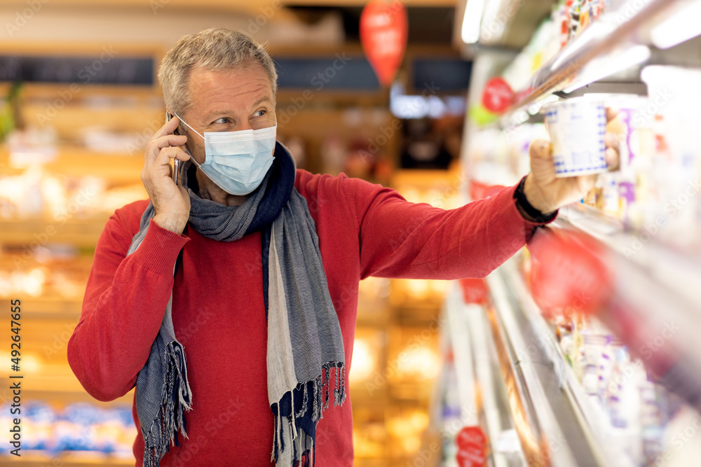 Senior man in face mask having phone conversation while shopping Senior man in face mask having phone conversation while shopping