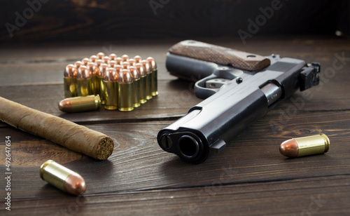 Legendary U.S. Army handgun Colt 1911A1 with .45 bullets and a cigar on wooden background, gangster mafia and war concept photo