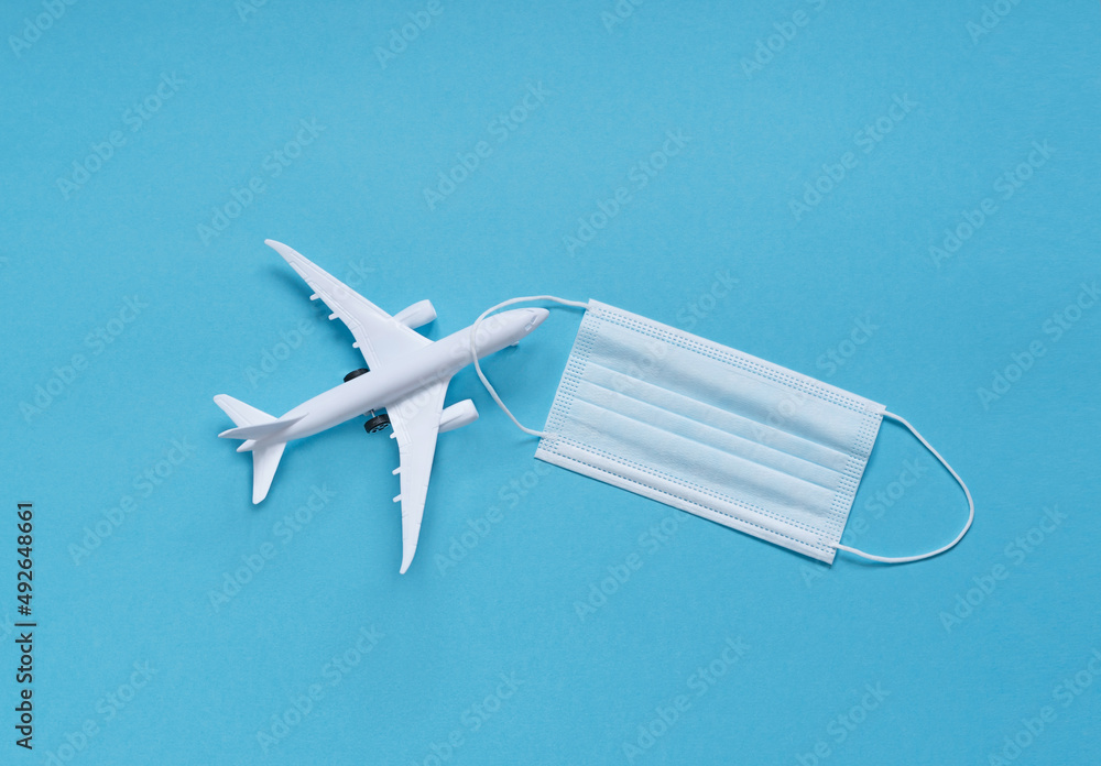 a white plane with a medical mask on a blue background. the concept of social distance. travel planning. a white plane with a medical mask on a blue background. the concept of social distance. travel planning.