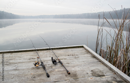 Fishing rod, spinning reel on the wooden background pier river bank. Sunrise. Misty fog against the backdrop of lake. Misty morning. wild nature. The concept of rural getaway. Article about fishi photo