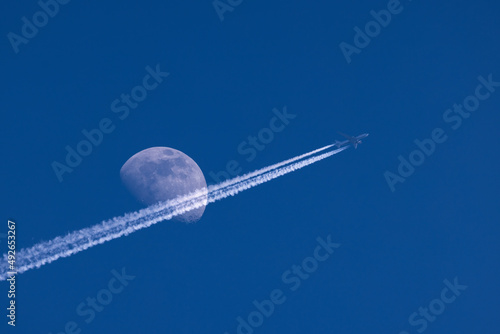 Plane flies pass over the moon on blue sky airplane trail