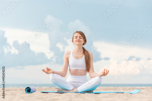 Yoga at sunrise on the beach. Young beautiful woman practicing yoga meditation outdoors by the sea