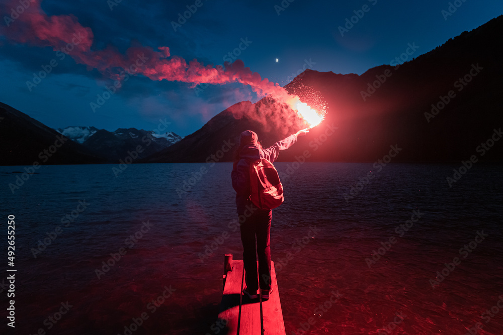 The hiker on the pier lit the emergency red torch and calling for help. Rescue flare and sos signal concept - obrazy, fototapety, plakaty 