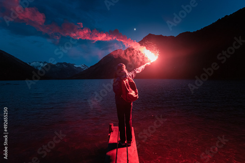 The hiker on the pier lit the emergency red torch and calling for help. Rescue flare and sos signal concept